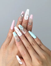 Hand model wearing coffin-shaped press-on nails in pastel pink and blue with crackle texture and starry moon details